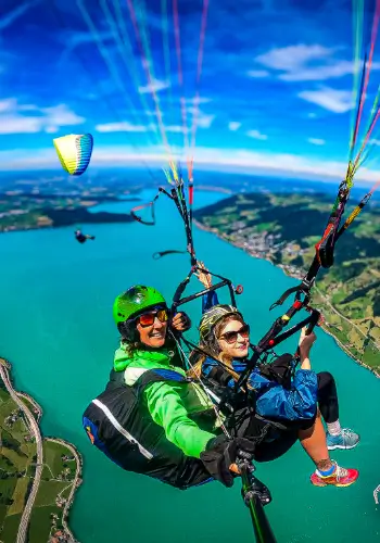 Passagierin fliegt am Tandem mit touch and go Paragliding, während ihr Freund mit seinem eigenen Gleitschirm nebenher fliegt.