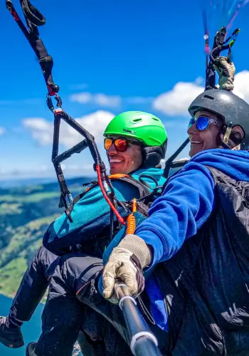 Passagier und Tandempilotin lachen gemeinsam während eines Tandemflugs bei touch and go Paragliding.