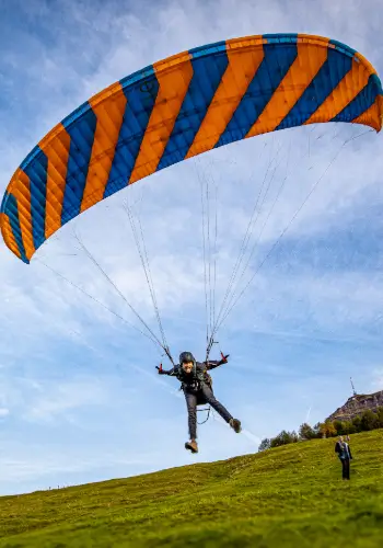 Ein Schüler hebt mit einem Phi-Gleitschirm ab und startet seinen ersten kleinen Flug am Übungshang unter Anleitung eines erfahrenen Fluglehrers.