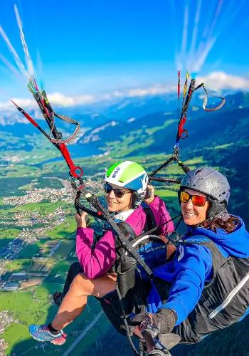 Tandempilot mit Flugschüler beim Gleitschirmflug über der beeindruckenden Berglandschaft und Seen der Zentralschweiz, umgeben von klarer Luft und atemberaubender Aussicht.