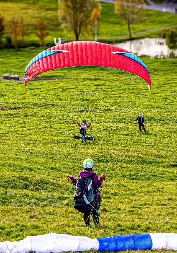 Ein Gleitschirmschüler startet zu seinem ersten kleinen Flug mit seinem Niviuk Gleitschirm am Übungshang, begleitet von einem erfahrenen Fluglehrer von der Flugschule touch and go Paragliding.