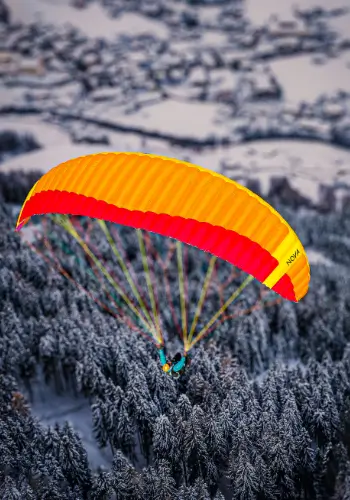 Ein Gleitschirmpilot fliegt über verschneite Wälder in der Zentralschweiz und geniesst die winterliche Landschaft aus der Vogelperspektive.