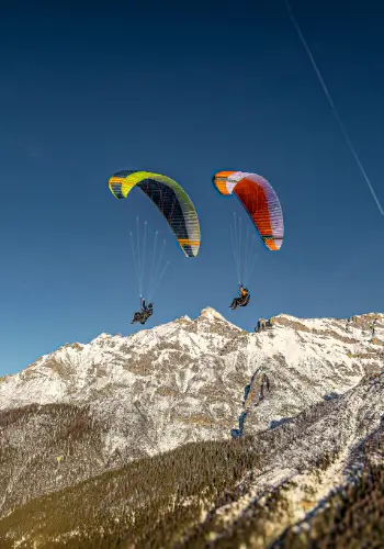 Gleitschirme fliegen vor der majestätischen Alpenkulisse während eines Paragliding-Erlebnisses mit touch and go Paragliding, der Flugschule in der Zentralschweiz.