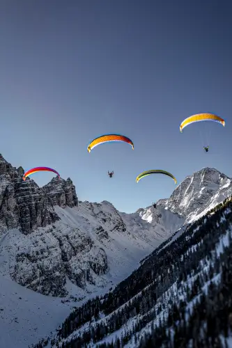 Vier Gleitschirme fliegen vor der majestätischen Alpenkulisse während eines Paragliding-Erlebnisses mit touch and go Paragliding.