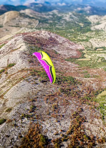 Gleitschirmpilot schwebt über den malerischen Hügeln Bosniens während der Bosnien Tour von touch and go Paragliding.