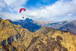 Gleitschirmpiloten fliegen über die grünen Hügel und felsigen Bergen von Bassano del Grappa beim Oster-Ausflug von touch and go Paragliding.