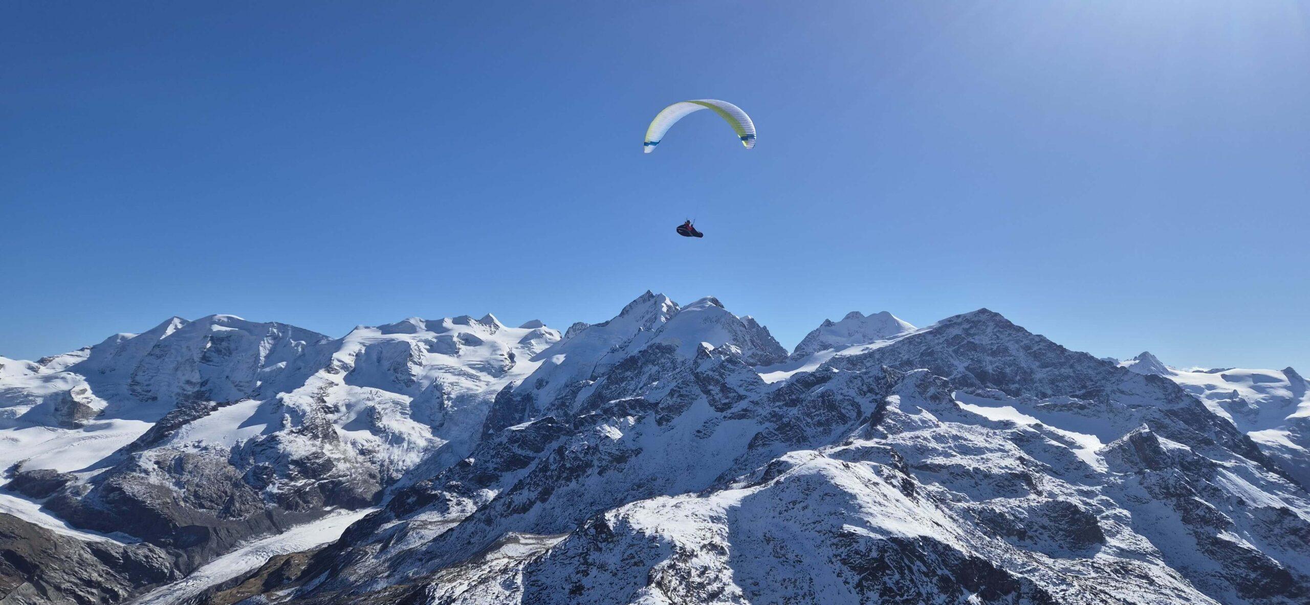 Gleitschirmpilot fliegt über den Engadiner Bergen mit weitem Blick auf die alpine Landschaft.